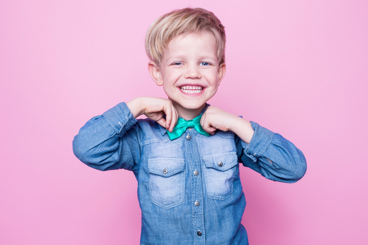 Young beautiful boy with blue shirt and butterfly tie. Studio portrait over pink background